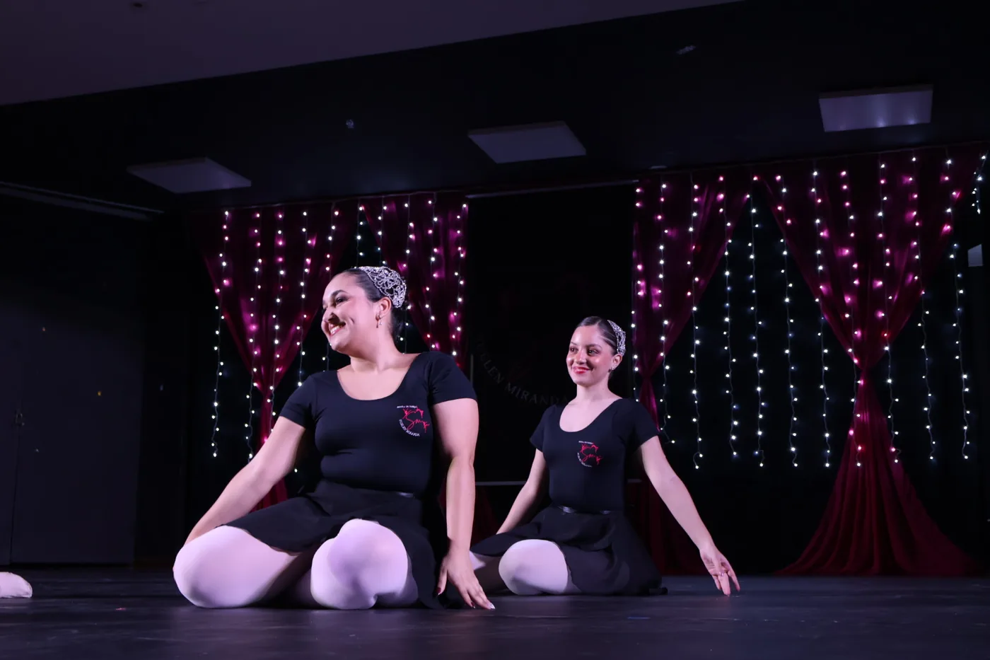 Duas alunas de ballet sentadas no palco, com o collant da escola
