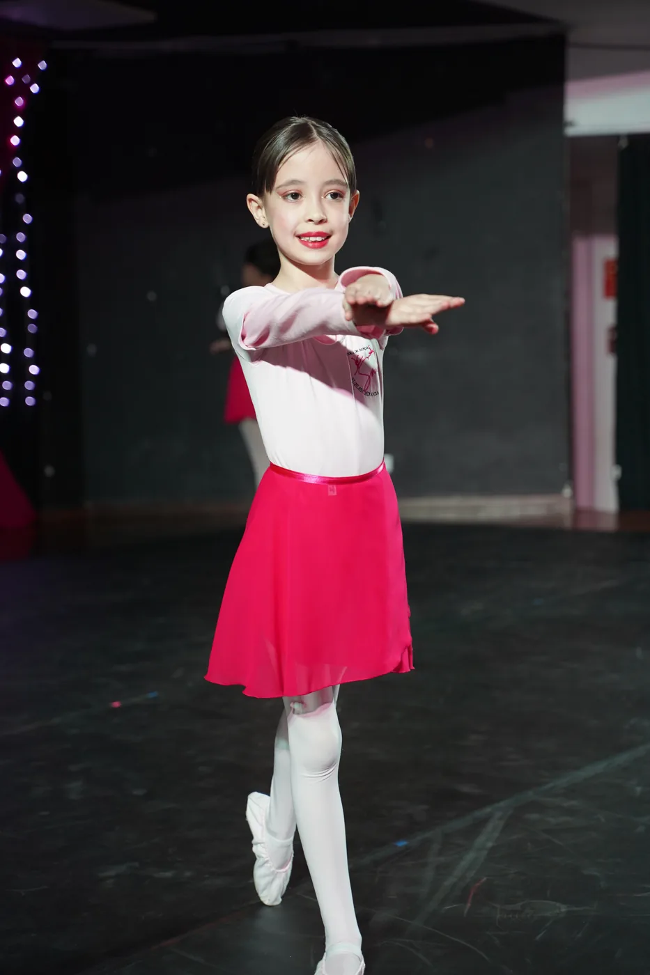 Aluna pequena de ballet em pose de aula, com collant e saia rosa