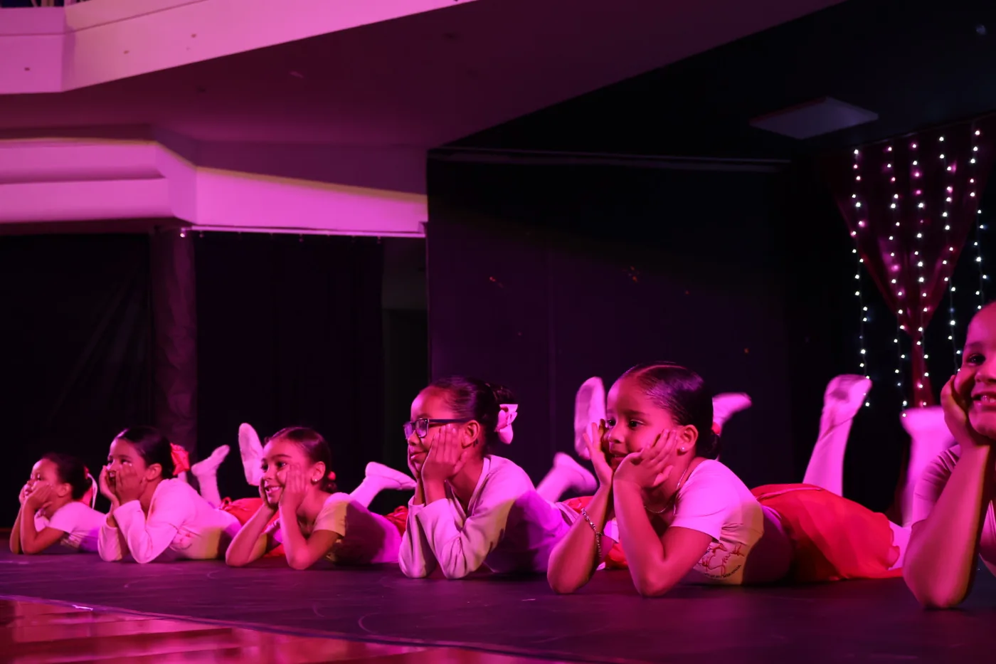 Alunas pequenas de ballet deitadas no palco, de tutu, sob luz rosa